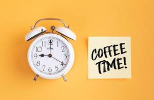 Wecker und ein Zettel mit ‘Coffee time!’ Text vor gelbem Hintergrund