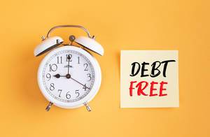 Wecker und ein Zettel mit ‘Debt-free’ Text vor gelbem Hintergrund