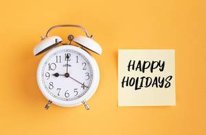 Wecker und ein Zettel mit ‘Happy holidays’ Text vor gelbem Hintergrund
