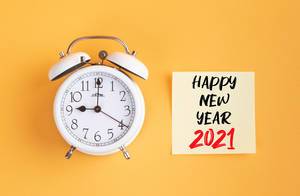 Wecker und ein Zettel mit ‘Happy new year 2021’ Text vor gelbem Hintergrund