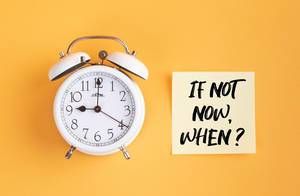 Wecker und ein Zettel mit ‘If not now, when?’ Text vor gelbem Hintergrund