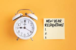 Wecker und ein Zettel mit ‘New year resolutions’ Text vor gelbem Hintergrund