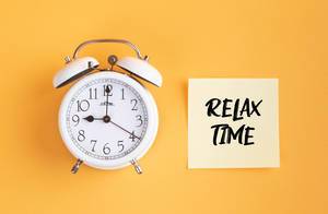 Wecker und ein Zettel mit ‘Relax time’ Text vor gelbem Hintergrund