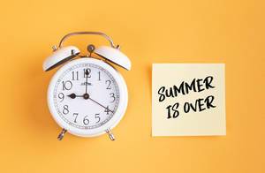 Wecker und ein Zettel mit ‘Summer is over’ Text vor gelbem Hintergrund