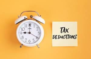 Wecker und ein Zettel mit ‘Tax deductions’ Text vor gelbem Hintergrund