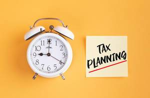 Wecker und ein Zettel mit ‘Tax planning’ Text vor gelbem Hintergrund
