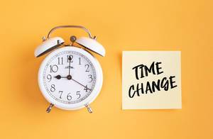 Wecker und ein Zettel mit ‘Time change’ Text vor gelbem Hintergrund