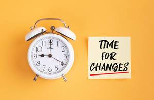 Wecker und ein Zettel mit ‘Time for changes’ Text vor gelbem Hintergrund