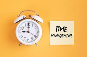 Wecker und ein Zettel mit ‘Time management’ Text vor gelbem Hintergrund