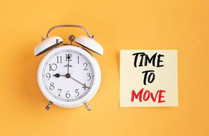 Wecker und ein Zettel mit ‘Time to move’ Text vor gelbem Hintergrund