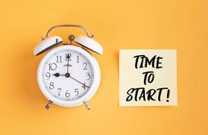 Wecker und ein Zettel mit ‘Time to start!’ Text vor gelbem Hintergrund