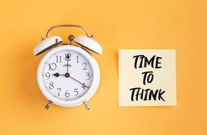 Wecker und ein Zettel mit ‘Time to think’ Text vor gelbem Hintergrund