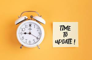 Wecker und ein Zettel mit ‘Time to update!’ Text vor gelbem Hintergrund