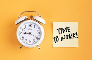 Wecker und ein Zettel mit ‘Time to work!’ Text vor gelbem Hintergrund