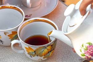 Weibliche Hand gießt Tee aus einer Teekanne in eine Tasse