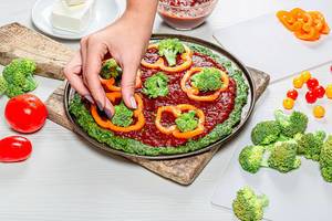 Weibliche Hände legen Stücke von Brokkoli auf den gesunden Pizzateig - das Konzept der gesunden Ernährung