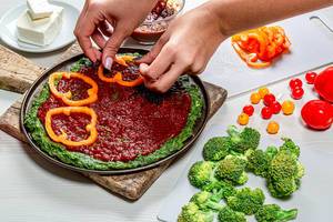 Weibliche Hände legen Stücke von Paprika auf den gesunden Pizzateig - das Konzept der gesunden Ernährung