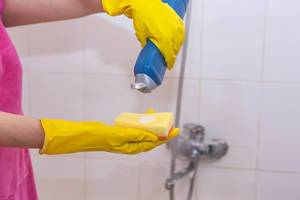 Weibliche Hände mit gelben Gummihandschuhen und einem Schwamm bei der Badreinigung