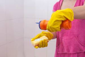 Weibliche Person mit Putzhandschuh und Putzmittel, reinigt das Bad