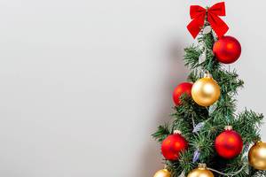 Weihnachtsbaum mit roten und golden Schmücken und mit einer Lichterkette im weißen Hintergrund