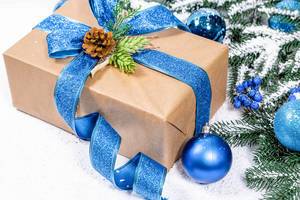 Weihnachtsgeschenk in Naturpapier mit blauem Band, Tannenzapfe, Baumkugeln, und Schnee