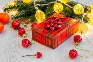 Weihnachtsgeschenk in roter Verpackung mit Tannenzweigen, roten Weihnachtsbällen und Mandarinen auf einem Holztisch