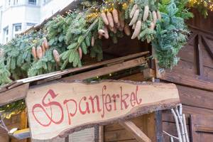 Weihnachtsmarktstand mit Spanferkel im Angebot, angepriesen auf Holzschild