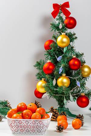 Weihnachtsstimmung: Ein geschmückter Mini-Weihnachtsbaum mit einer Schachtel Mandarinen und einigen Zapfen