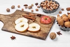 Weihnachtsstimmung: Verschiedene Nüsse, geschnittene Äpfel und Gewürze auf Holztisch
