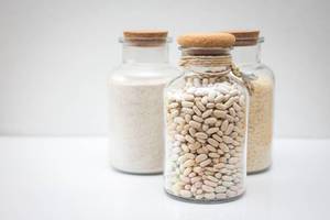 Weiße Bohnen, Reis und Mehl in Gläsern mit Korken auf weißem Hintergrund