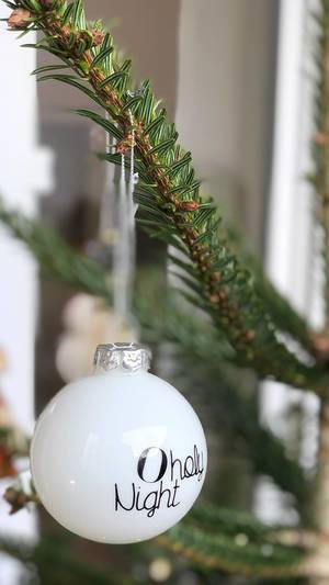 Weiße Weihnachtsbaumkugel mit der Aufschrift "O holy Night" hängt an einem grünen Zweig