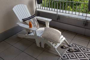 Weißer Liegestuhl mit gemütlichen Kissen, Sommerschlappen und Sonnenmilch, auf einem Balkon