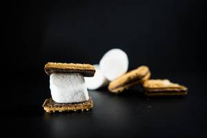 Weißes Marshmallow in Keks mit Schokoladenglasur vor auf schwarzem Hintergrund