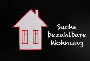 Weißes Papier-Haus mit roter Umrandung auf schwarzem Hintergrund & Text "Suche bezahlbare Wohnung", zum Thema Mietpreiserhöhung