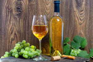 Weißwein, frische Weintrauben und ein Korkenzieher, vor einem dunklen Holzhintergrund