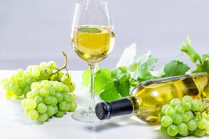 Weißwein im Weinglas, eine volle Weinflasche, Trauben und Blätter auf weißer Holzoberfläche