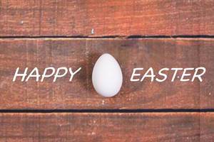 White chicken egg with Happy Easter text on wooden background