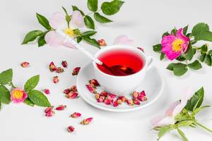 White cup of tea with dried and fresh tea rose flowers on a white background