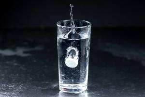 White effervescent Tablet dropping in a Glass of Water on dark Background