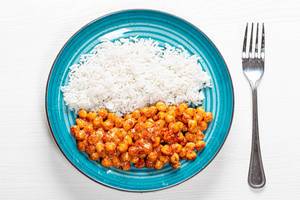White rice and chickpeas in tomato sauce on white wooden background with fork. Top view