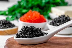 White spoon with black caviar, red and black caviar in bowls behind