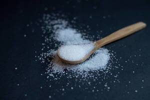 White sugar on a wooden spoon on dark background
