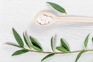 White tablets in a wooden spoon and a branch with green leaves on a white wooden background (Flip 2019)