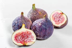 Whole and halves of fresh figs with water drops on white wooden background