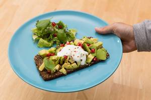 Whole grain bread with avocado and pomegranate on a blue plate
