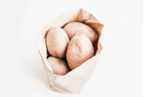 Whole raw potatoes in paper bag on white background