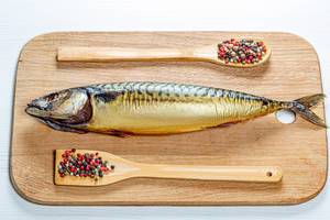 Whole smoked mackerel on a wooden kitchen Board with a mix of peppers. Top view