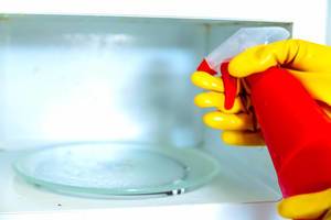 Woman hands in rubber gloves washing microwave