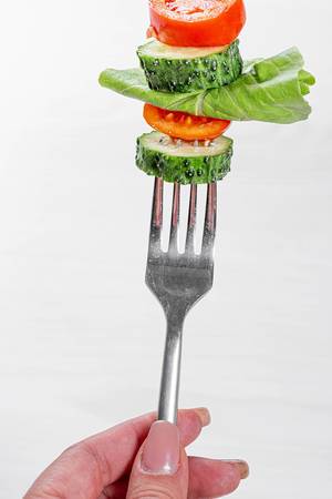 Woman holding a fork with fresh vegetables. Healthy eating concept
