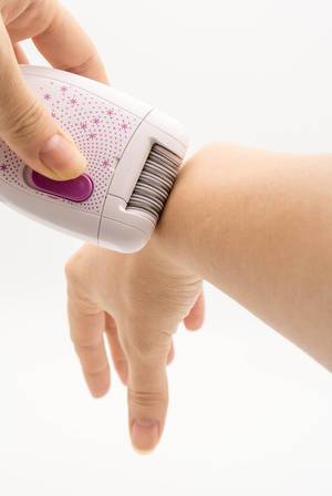 Woman removing hair from her arm with an epilator